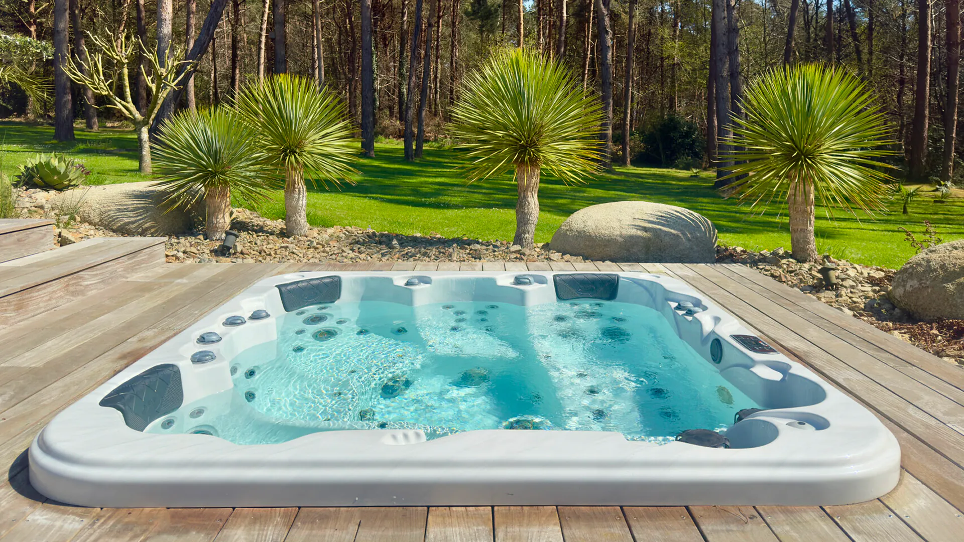 Spa blanc encastré dans une terrasse en bois au milieu d’un jardin paysagé