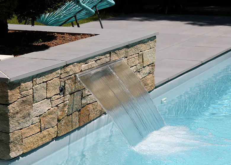 Lame d’eau transparente sur muret en pierre naturelle se déversant dans une piscine