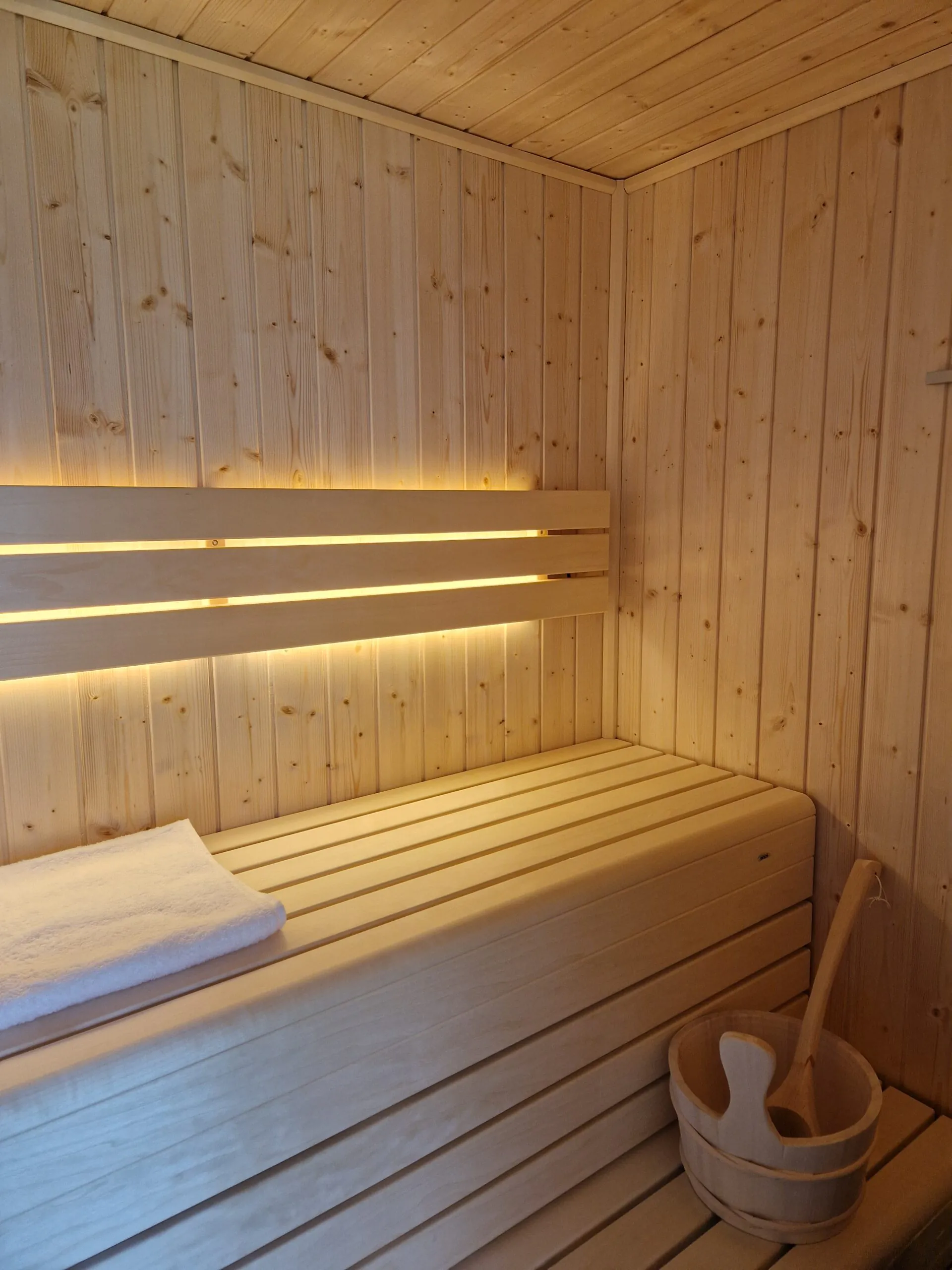 Intérieur de sauna en bois clair à Saint-Pever avec éclairage LED et seau