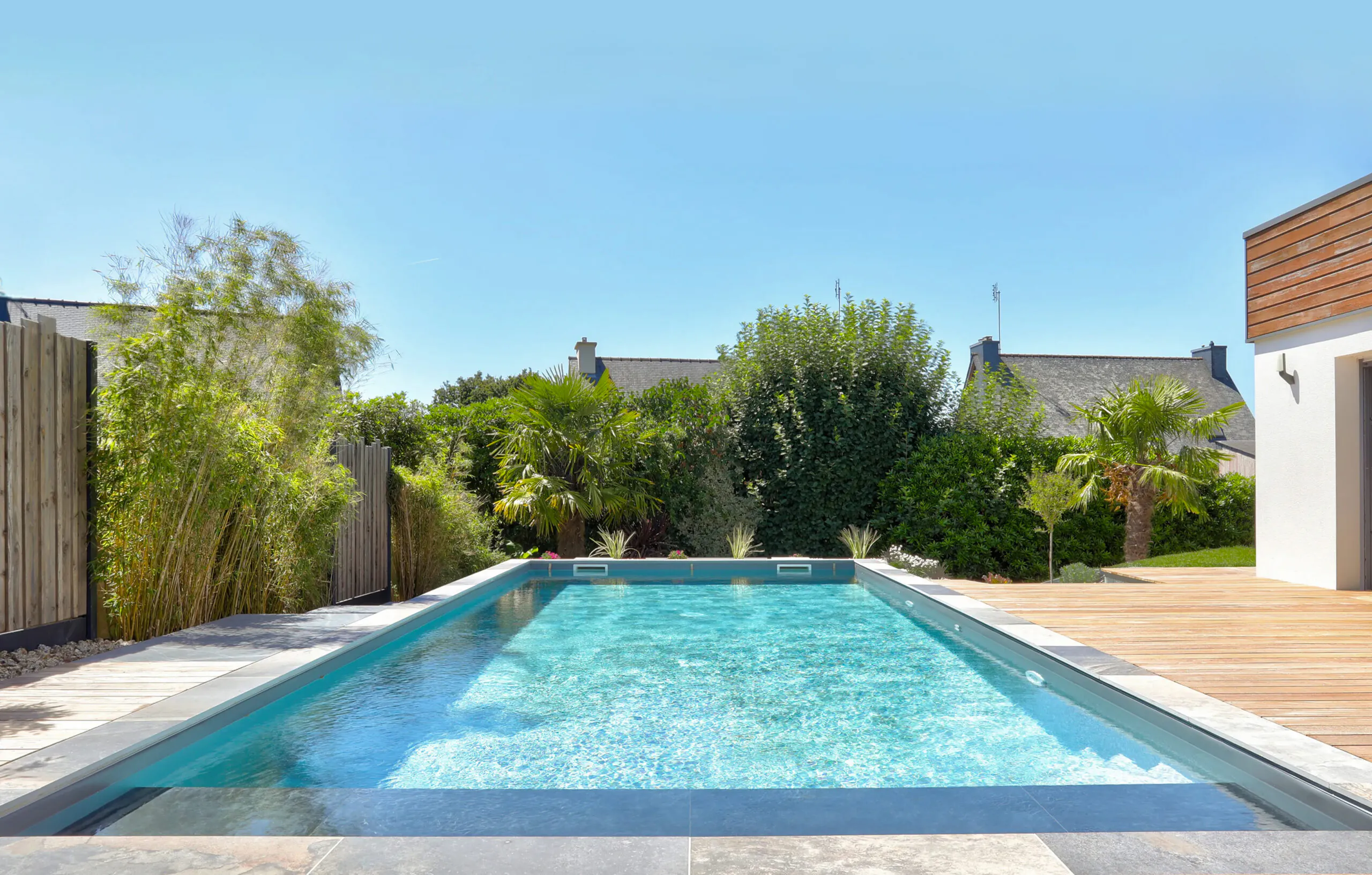 Piscine rectangulaire avec terrasse en bois et jardin paysager en Bretagne